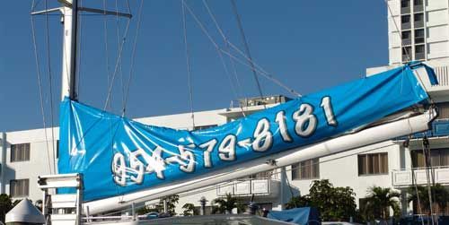 A blue sail is hanging from a sailboat with a phone number on it.