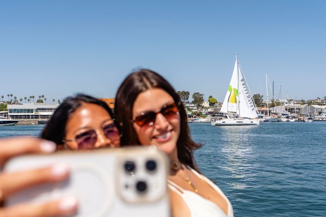 Two people taking a selfie on a boat with a sailboat and blue water in the background