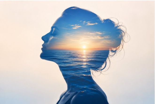 Silhouette of a woman’s profile with a sunset and ocean blended inside against a soft sky background