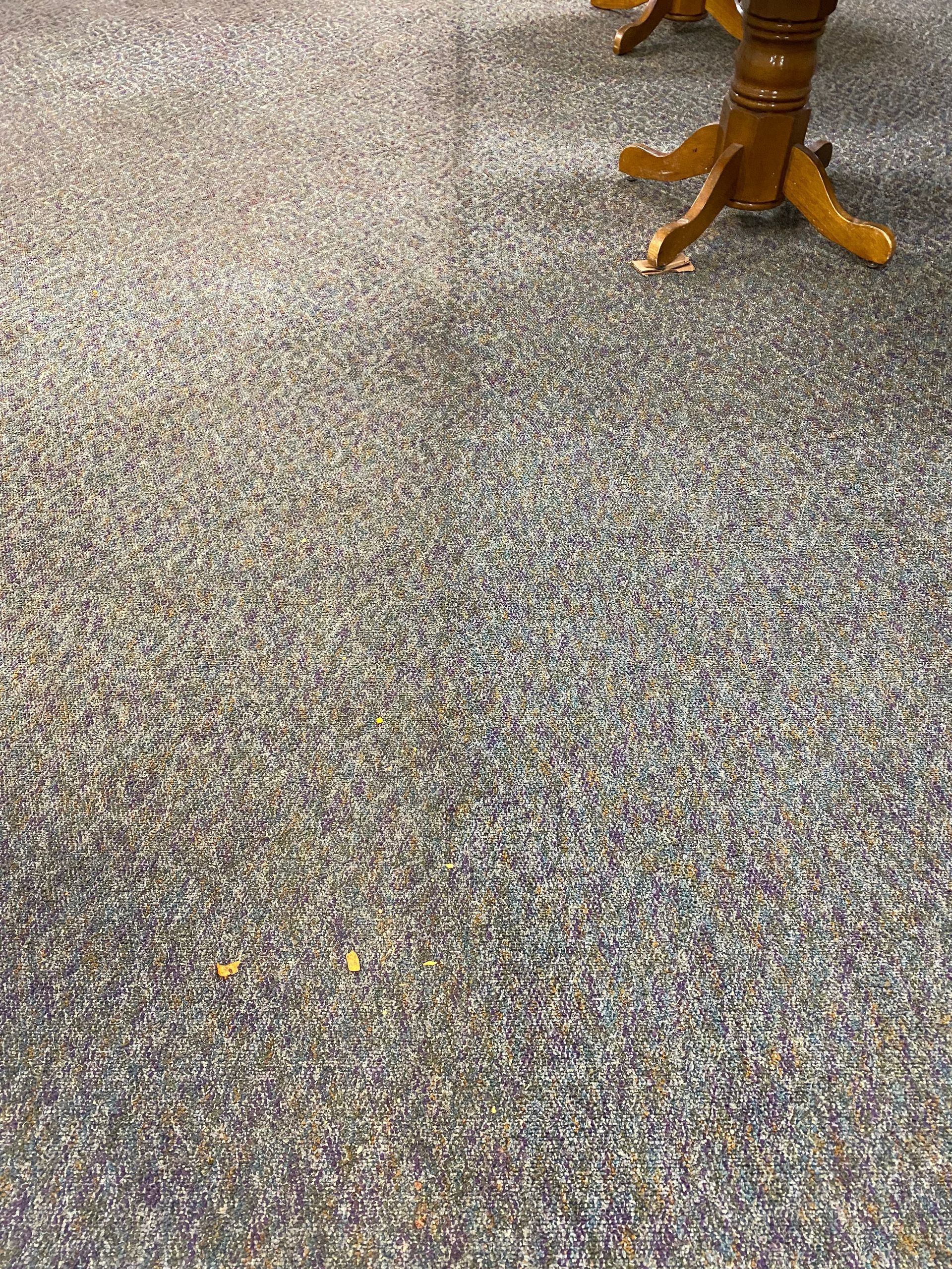 A close up of a carpeted floor with a table in the background.