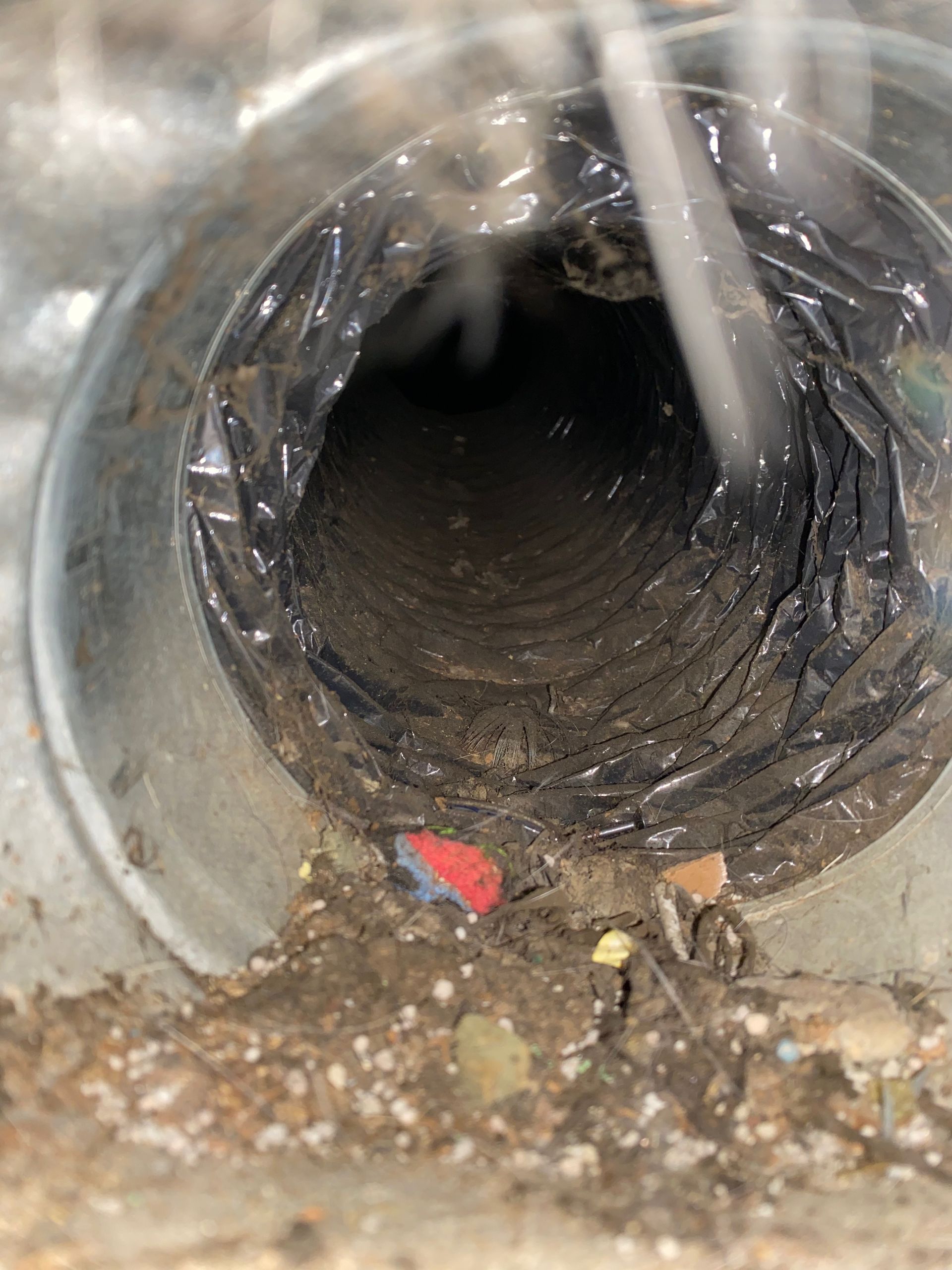 A close up of a dirty duct with a hose coming out of it.