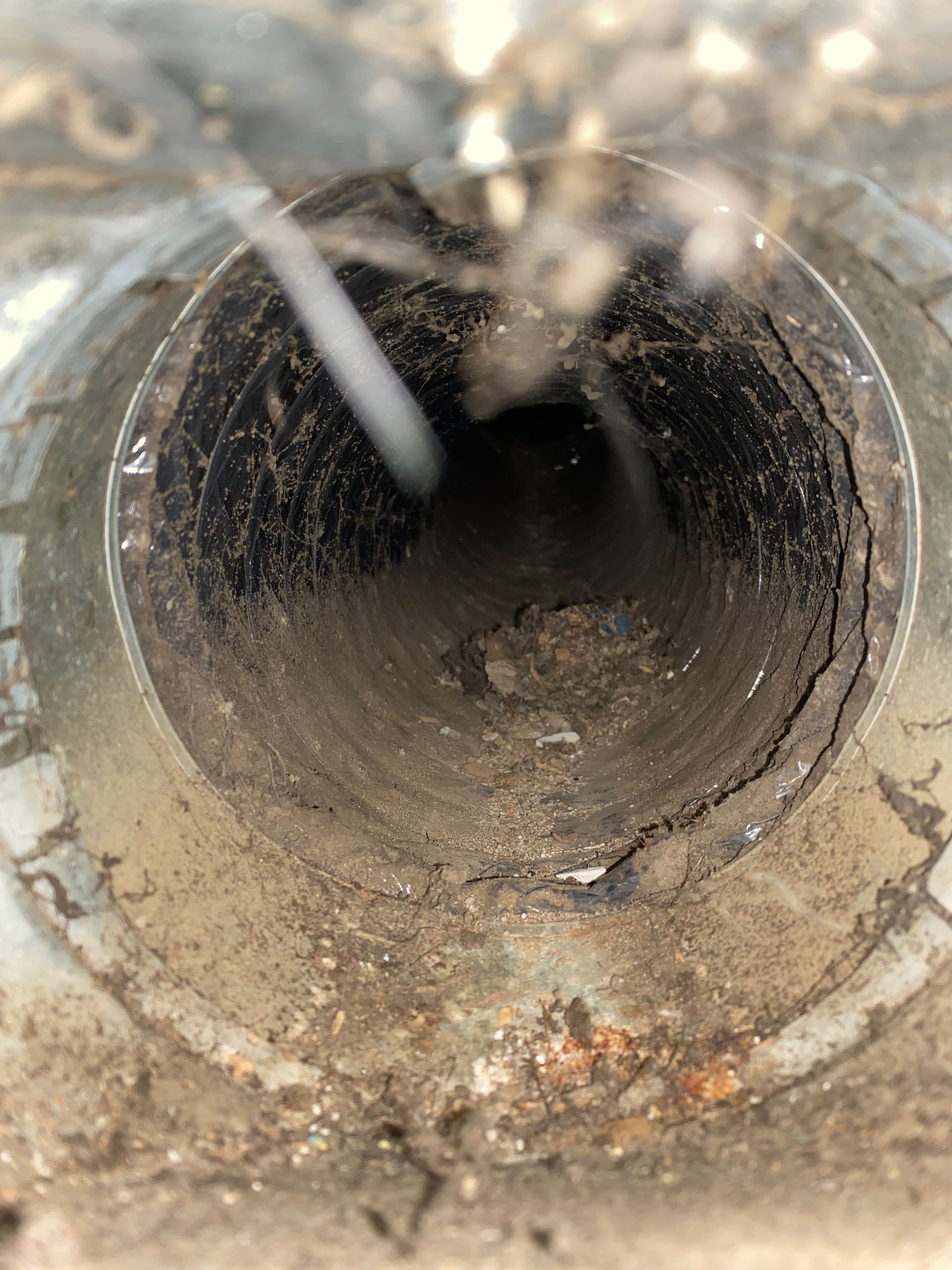 A close up of a dirty pipe with a hose coming out of it.