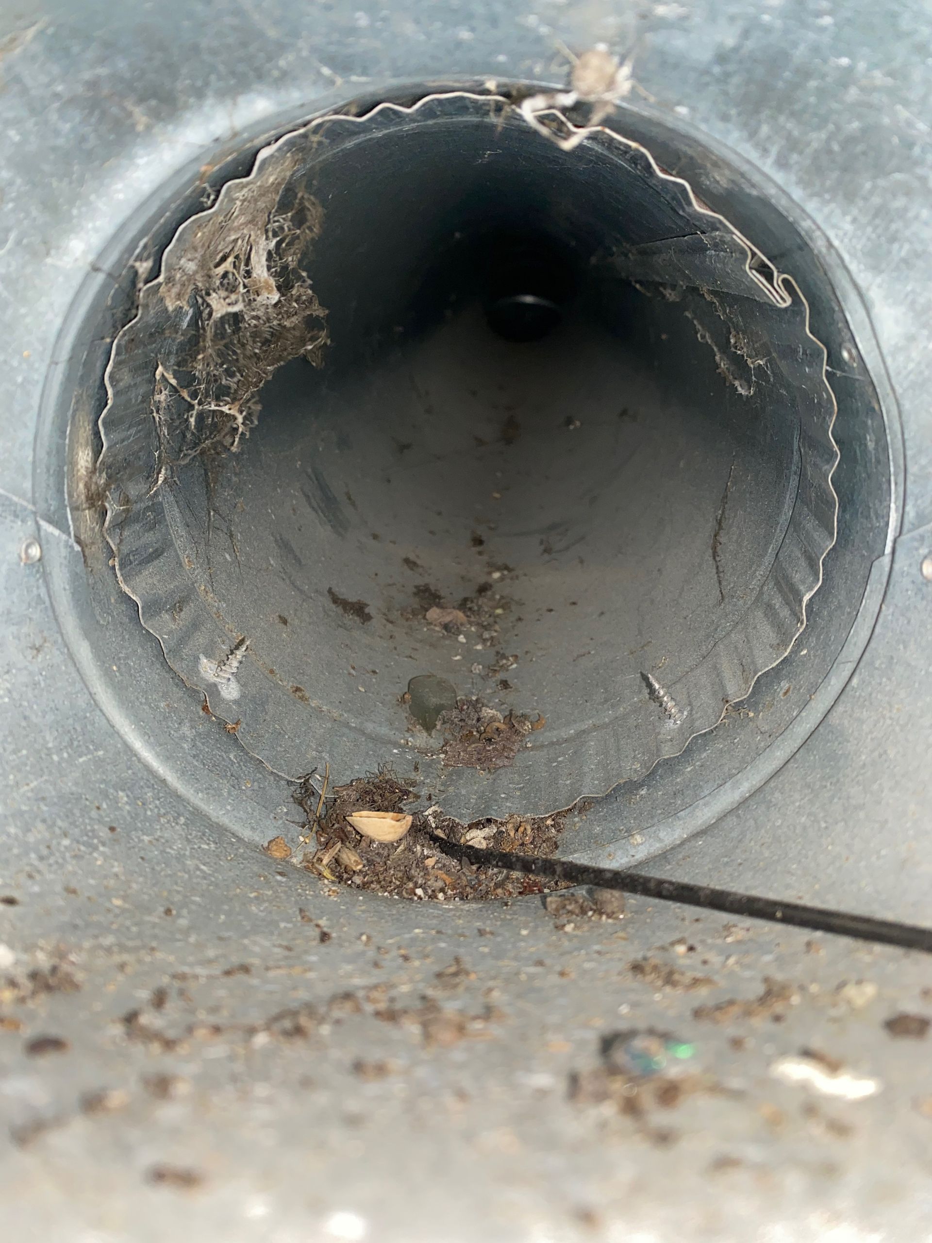 A close up of a dirty pipe with a wire sticking out of it.