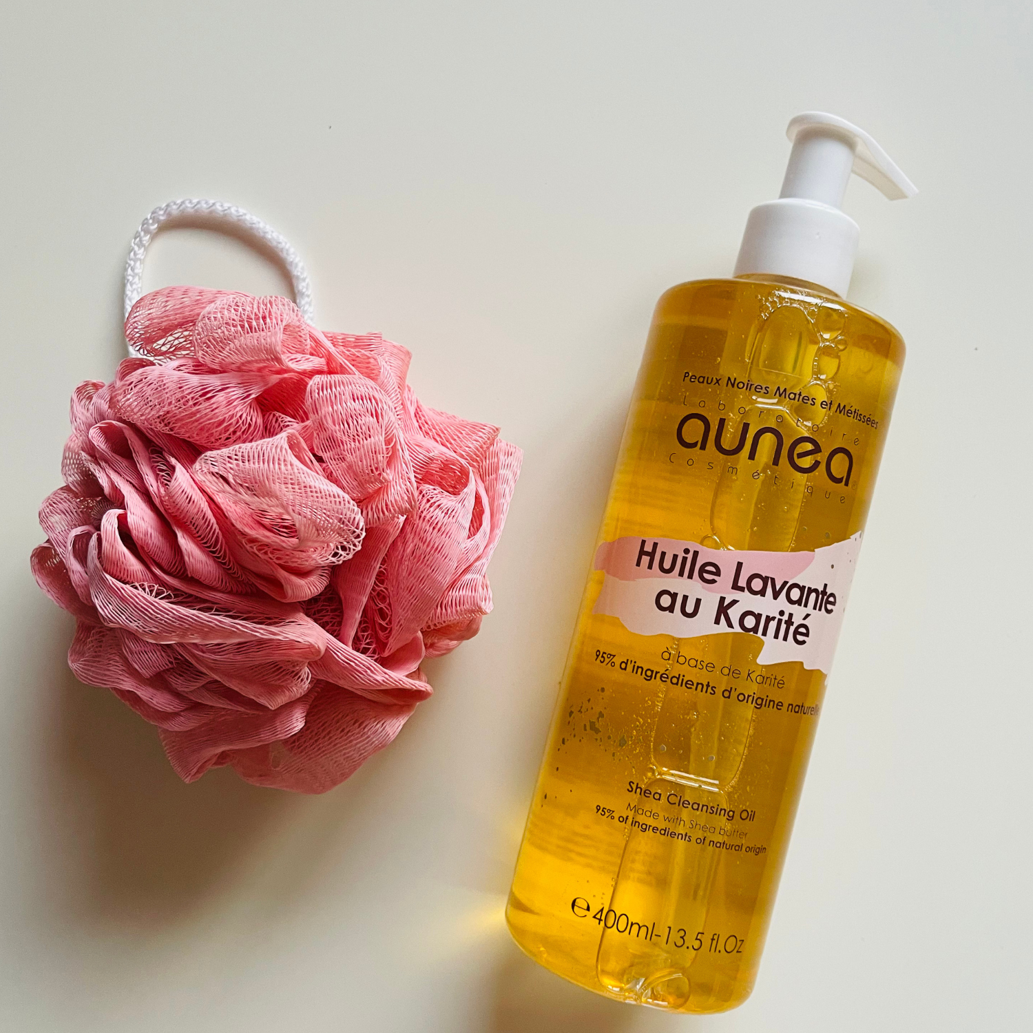Bouteille de crème de douche avec éponge de bain rose sur une surface texturée.