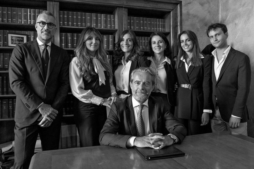 Sei persone in posa in un ufficio, una seduta a una scrivania e cinque in piedi dietro di lei.