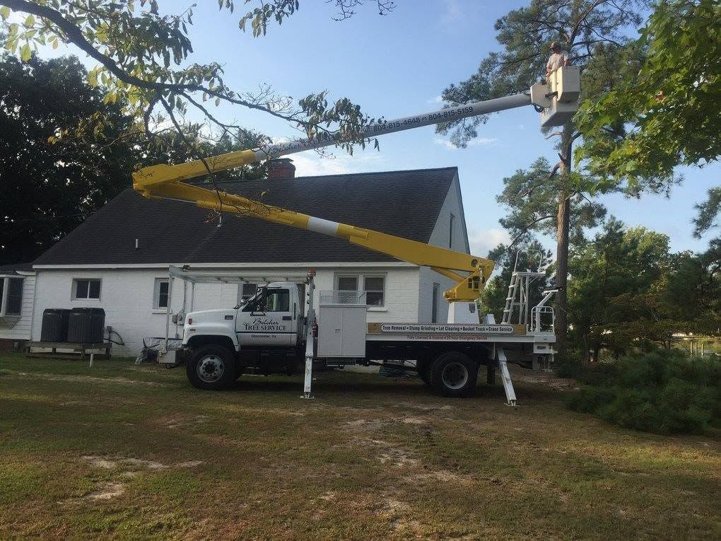 White utility truck with an extended boom lift parked beside a house under trees.