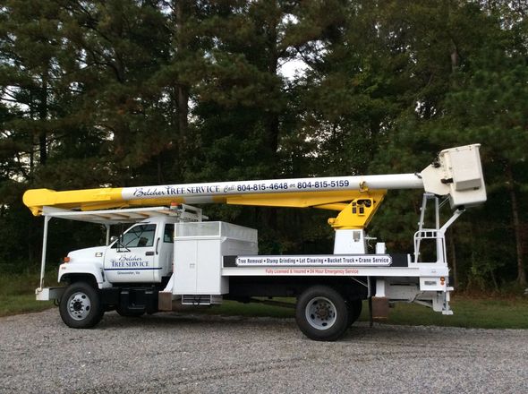White utility bucket truck with yellow boom parked on gravel by trees.