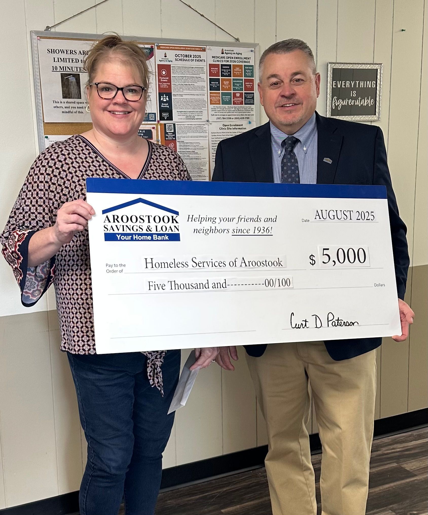 A woman and a man holding a large $5,000 donation check from Aroostook Savings & Loan for Homeless Services of Aroostook.