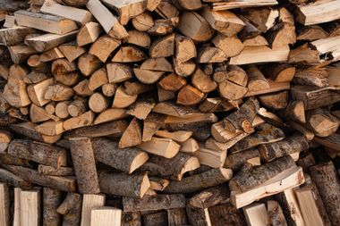 Stacked chopped firewood in a rustic pile, with brown logs filling the frame.