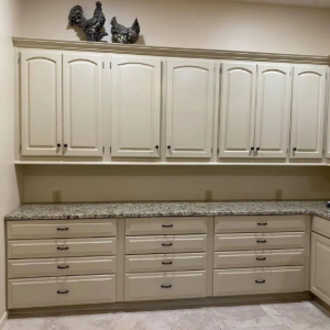 Beige kitchen with upper and lower cabinets, granite countertop, and decorative rooster figurines above the cabinets.