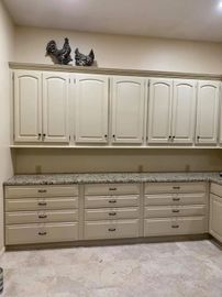 Built-in beige cabinets with granite countertop and decorative cat figurines above, in a tiled laundry room.