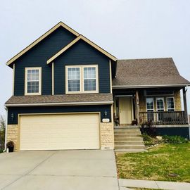 Two-story suburban house with blue siding, beige garage, front steps, and a small lawn