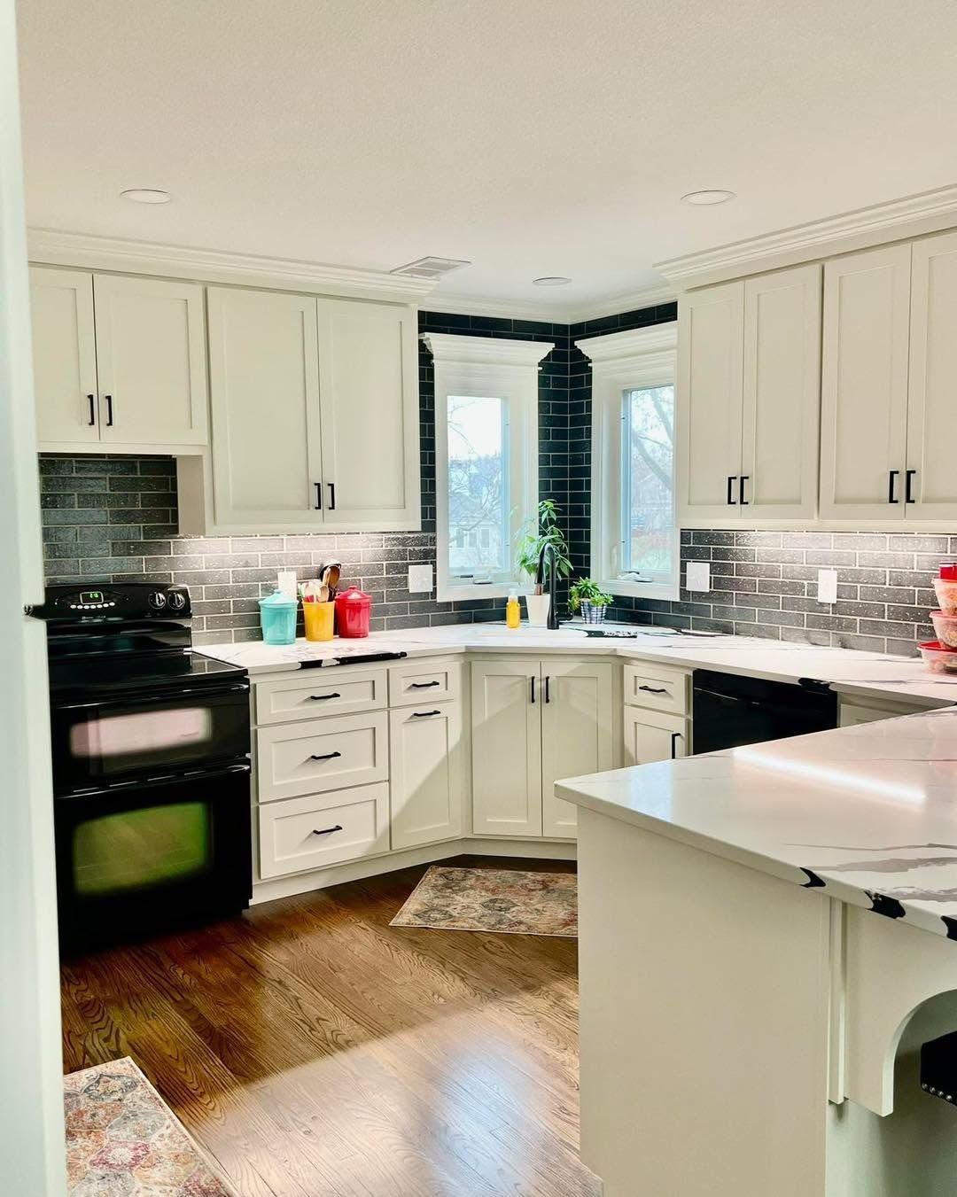 Bright white kitchen with black stove, marble countertops, and a bay window over the sink.