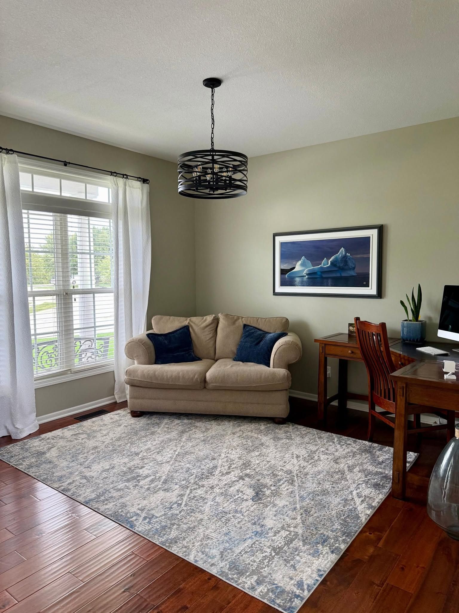 Living room with beige sofa, patterned rug, wood floor, and desk by a large window