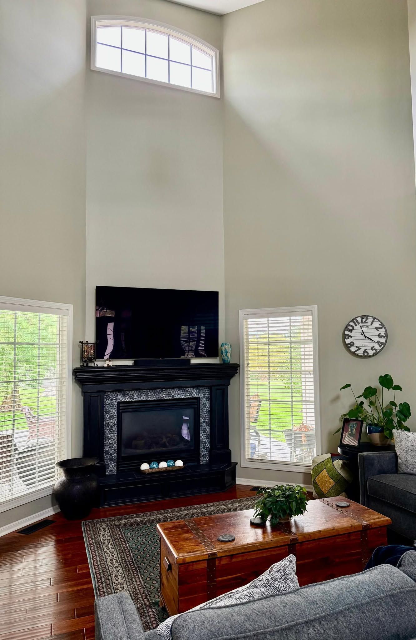 Living room with tall windows, black fireplace, wood coffee table, gray sofa, and wall clock