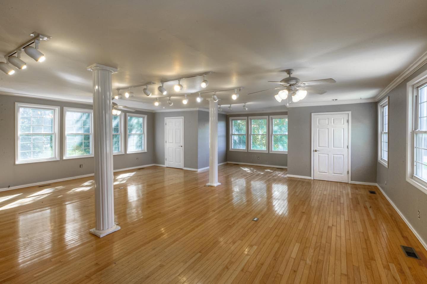 Empty bright room with hardwood floors, white columns, and large windows