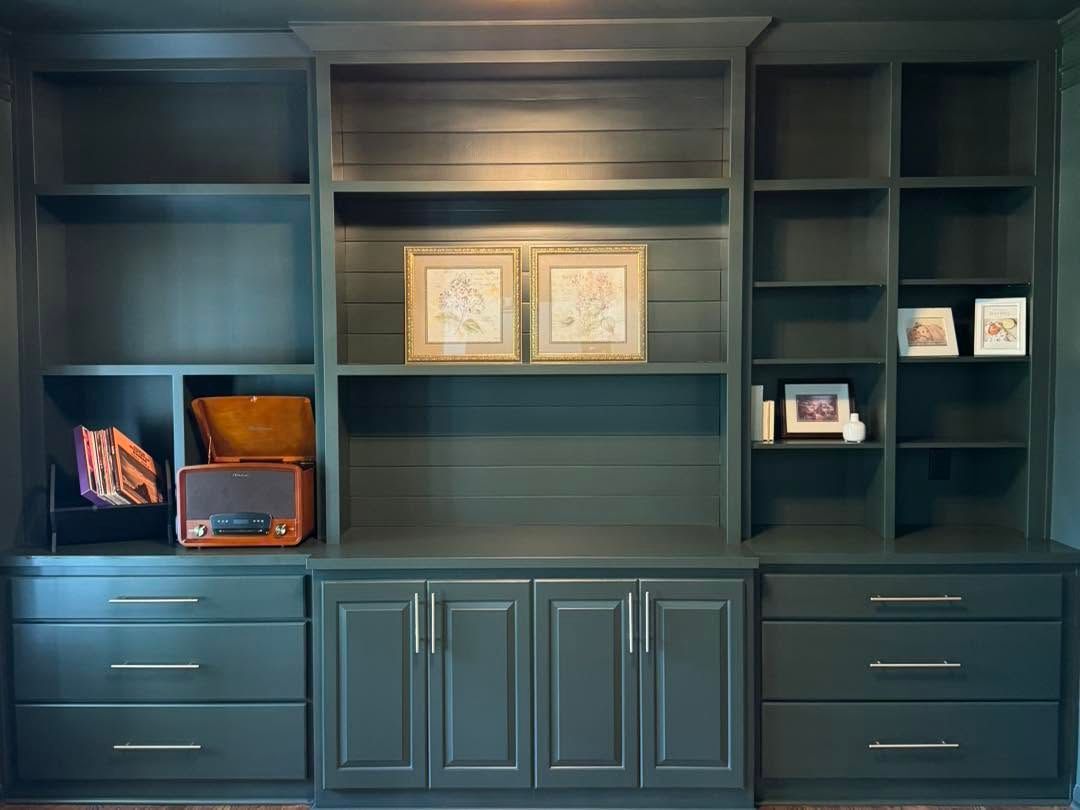 Built-in dark blue shelving and cabinets with framed art, a record player, and small decor items.