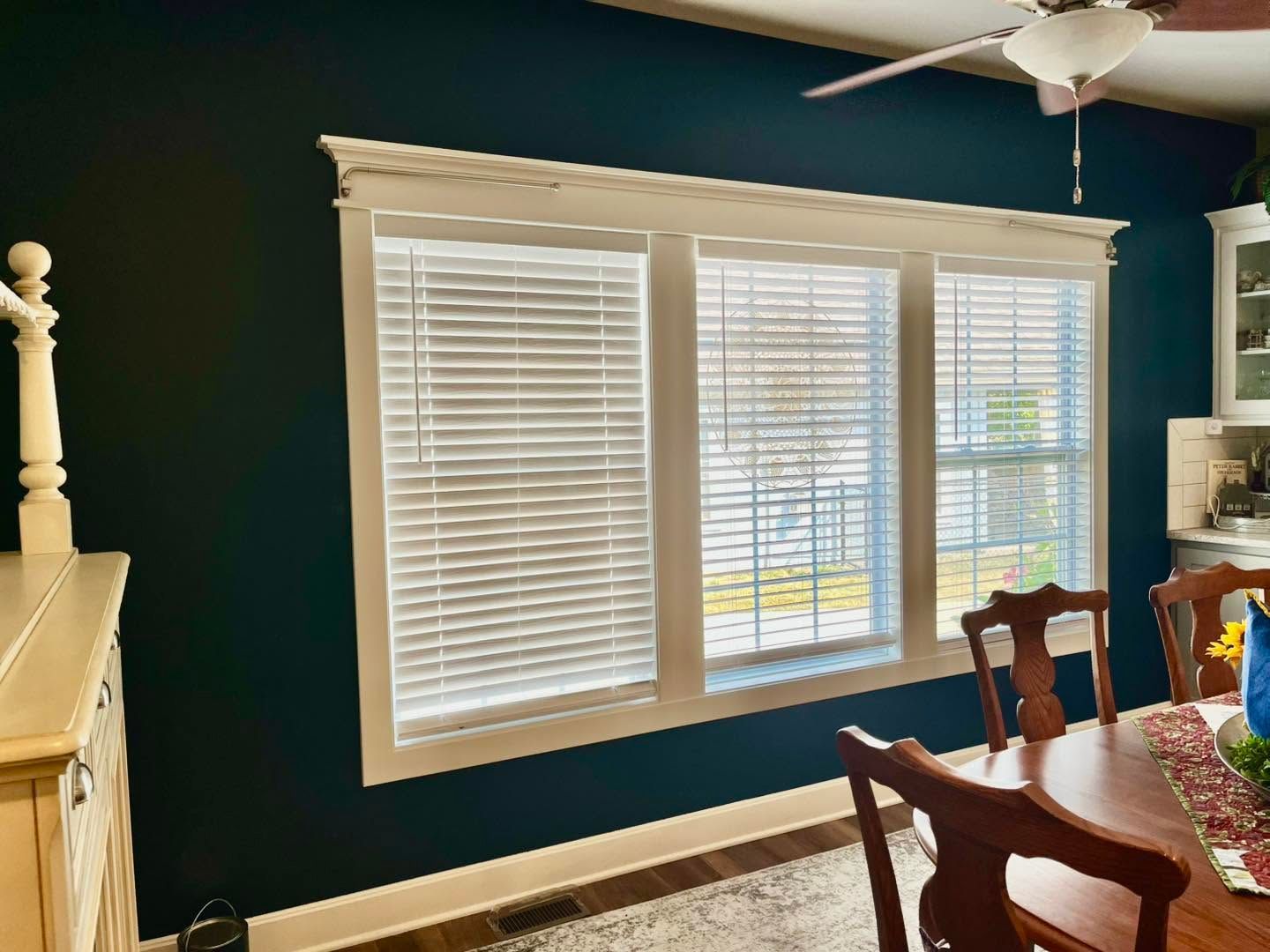 Dining room with teal walls, white blinds, ceiling fan, and wooden table by a bright window