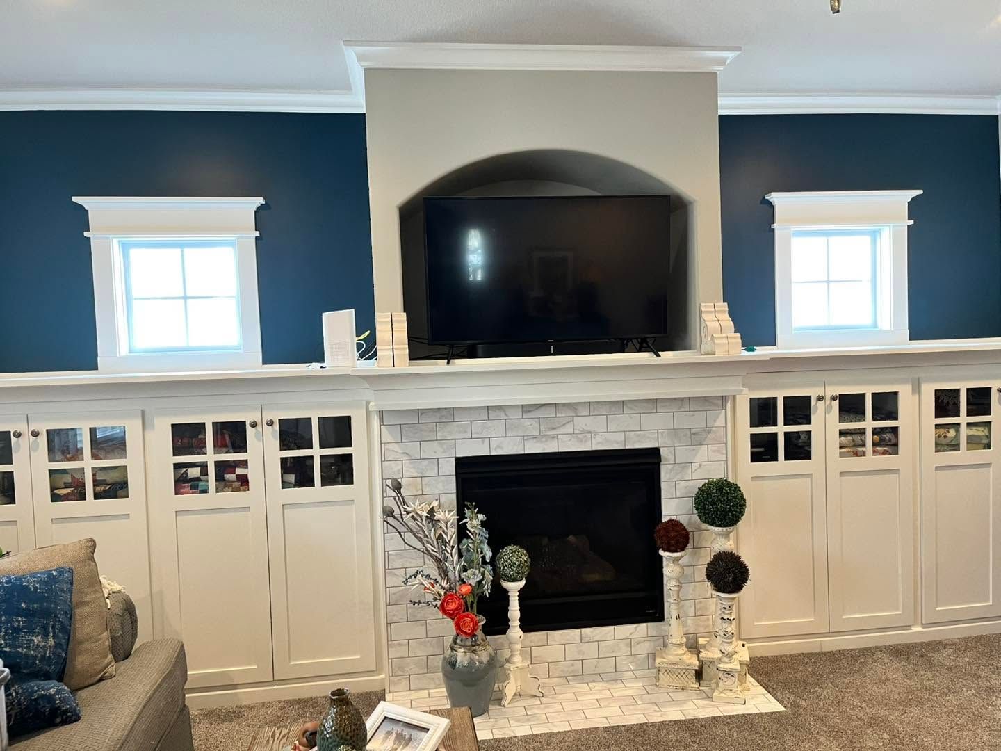 Living room with a white fireplace, built-in cabinets, blue walls, and a large TV above the mantel