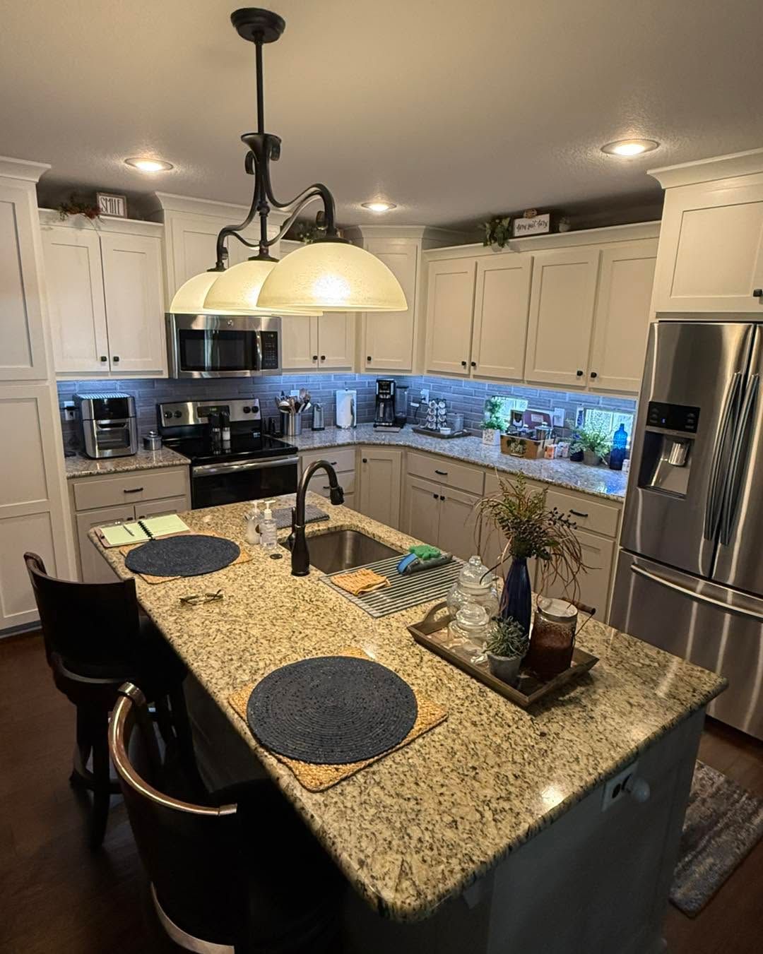 Modern kitchen with granite island, pendant lights, stainless appliances, and white cabinets