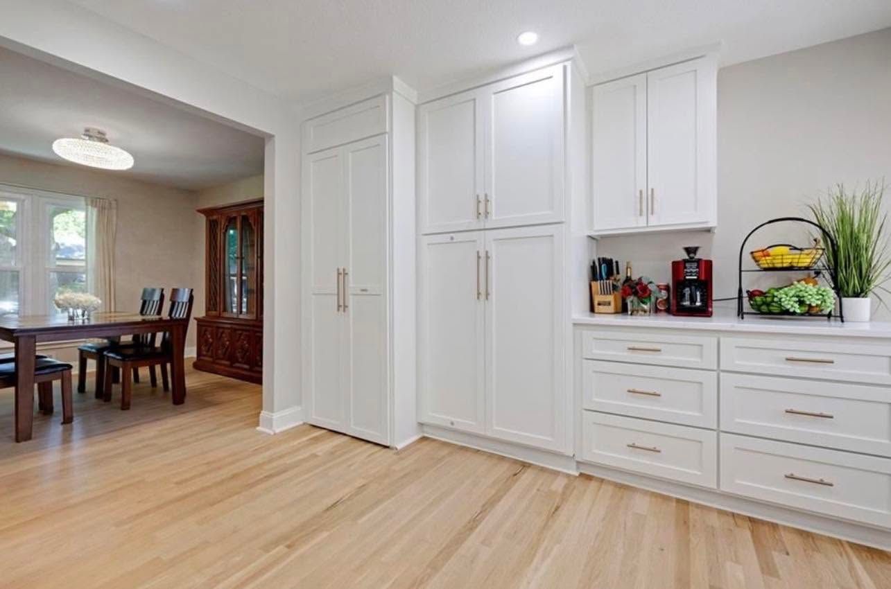Bright modern kitchen with white cabinets, light wood floors, and a dining room visible through an open doorway