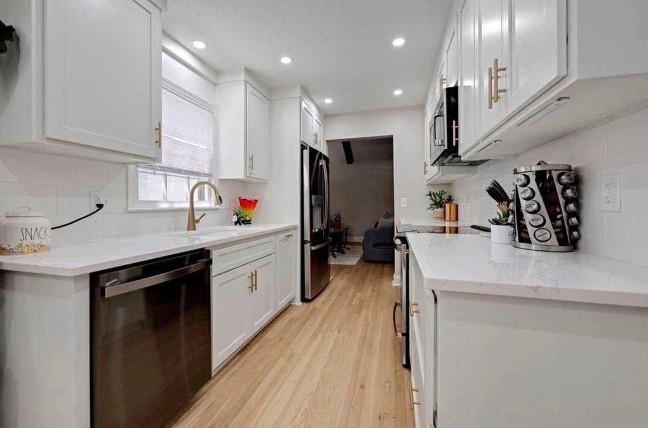 Bright white galley kitchen with wood floor, black dishwasher, and recessed ceiling lights