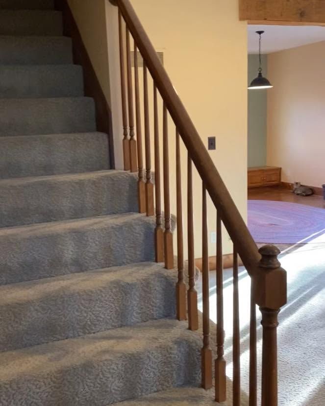Carpeted staircase with wooden railing in a home interior, leading to a room with a hanging light.