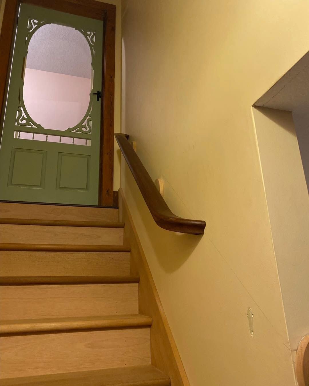 Staircase with beige walls, wooden steps, and a green door at the top.