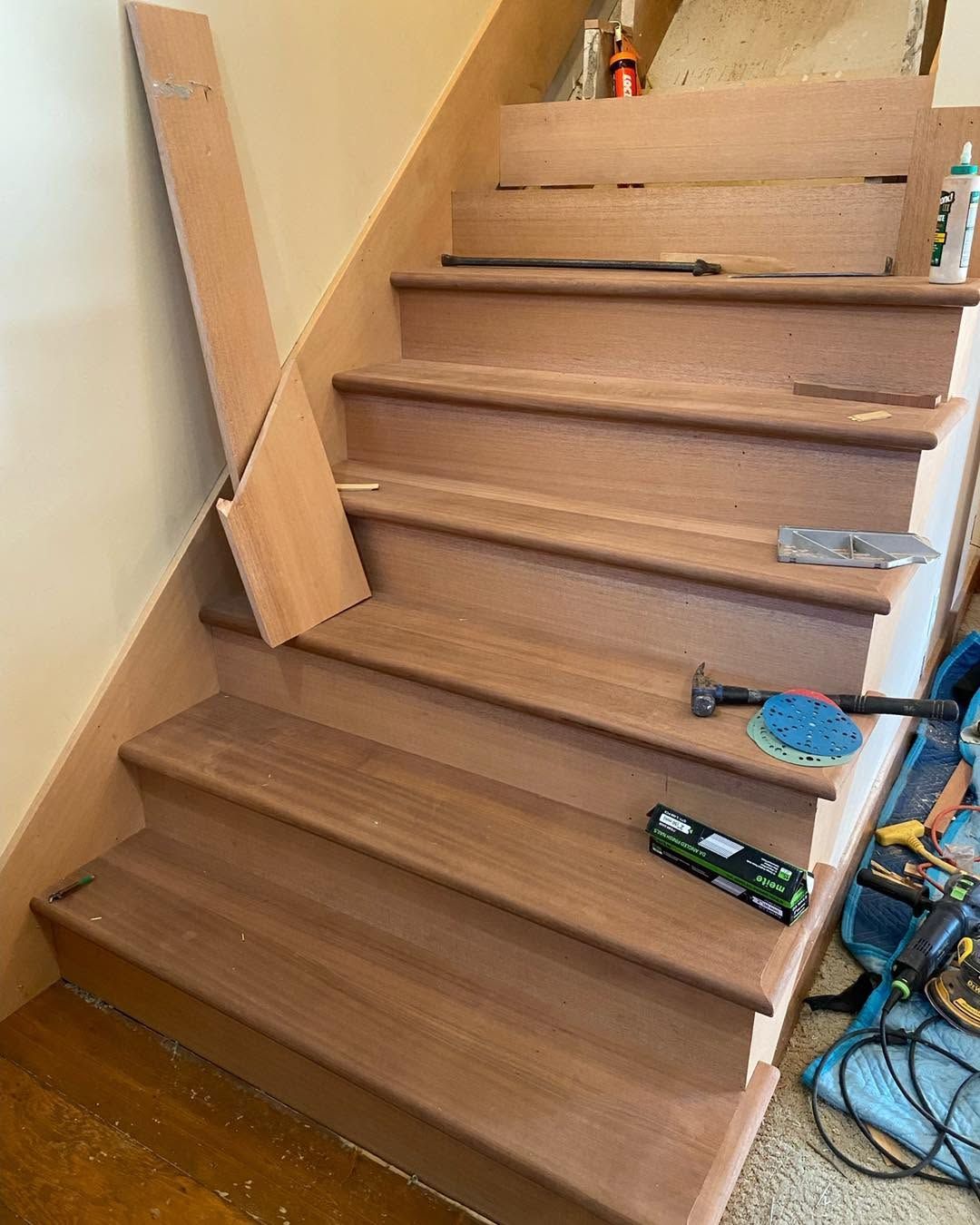 Wooden staircase under construction with loose boards, tools, and cables along the sides