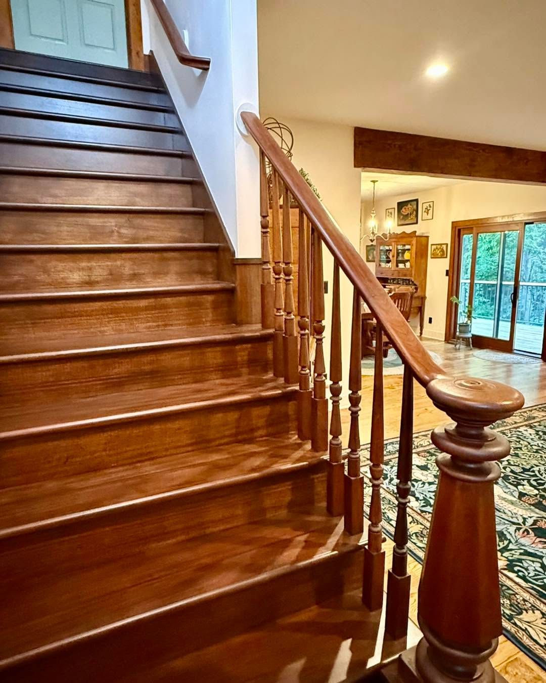 Wooden staircase with polished banister in a warmly lit home interior.