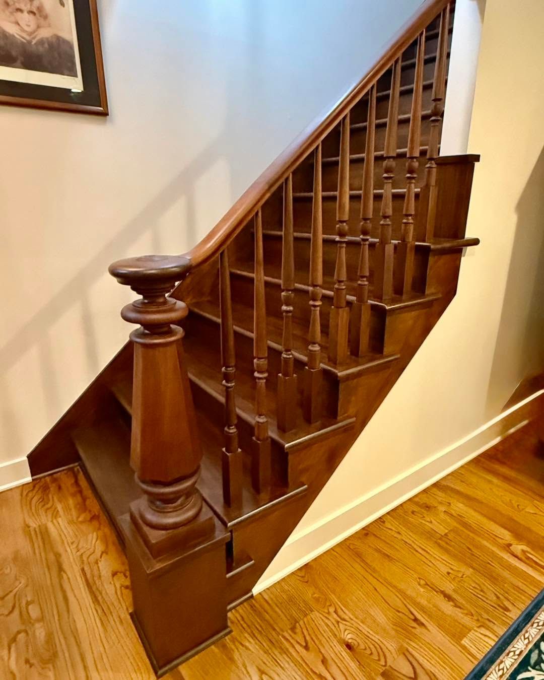 Wooden staircase railing and balusters beside a hardwood floor in a hallway