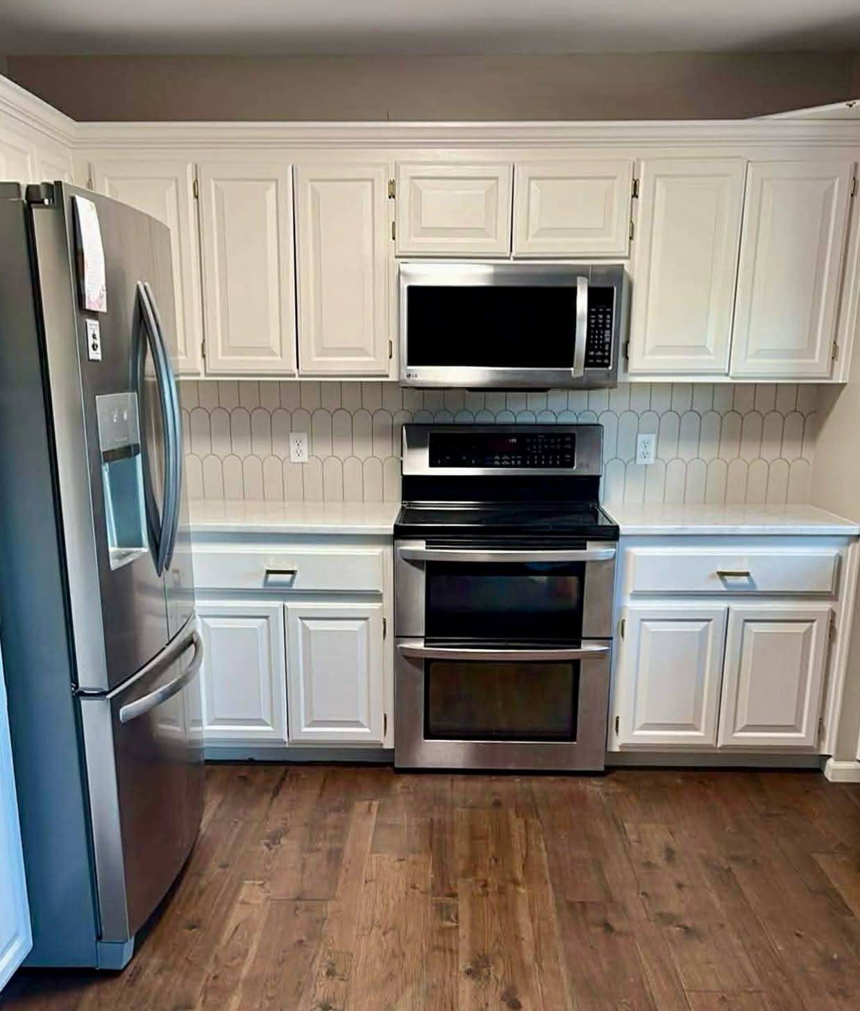 Modern kitchen with stainless steel appliances, white cabinets, and hardwood floor
