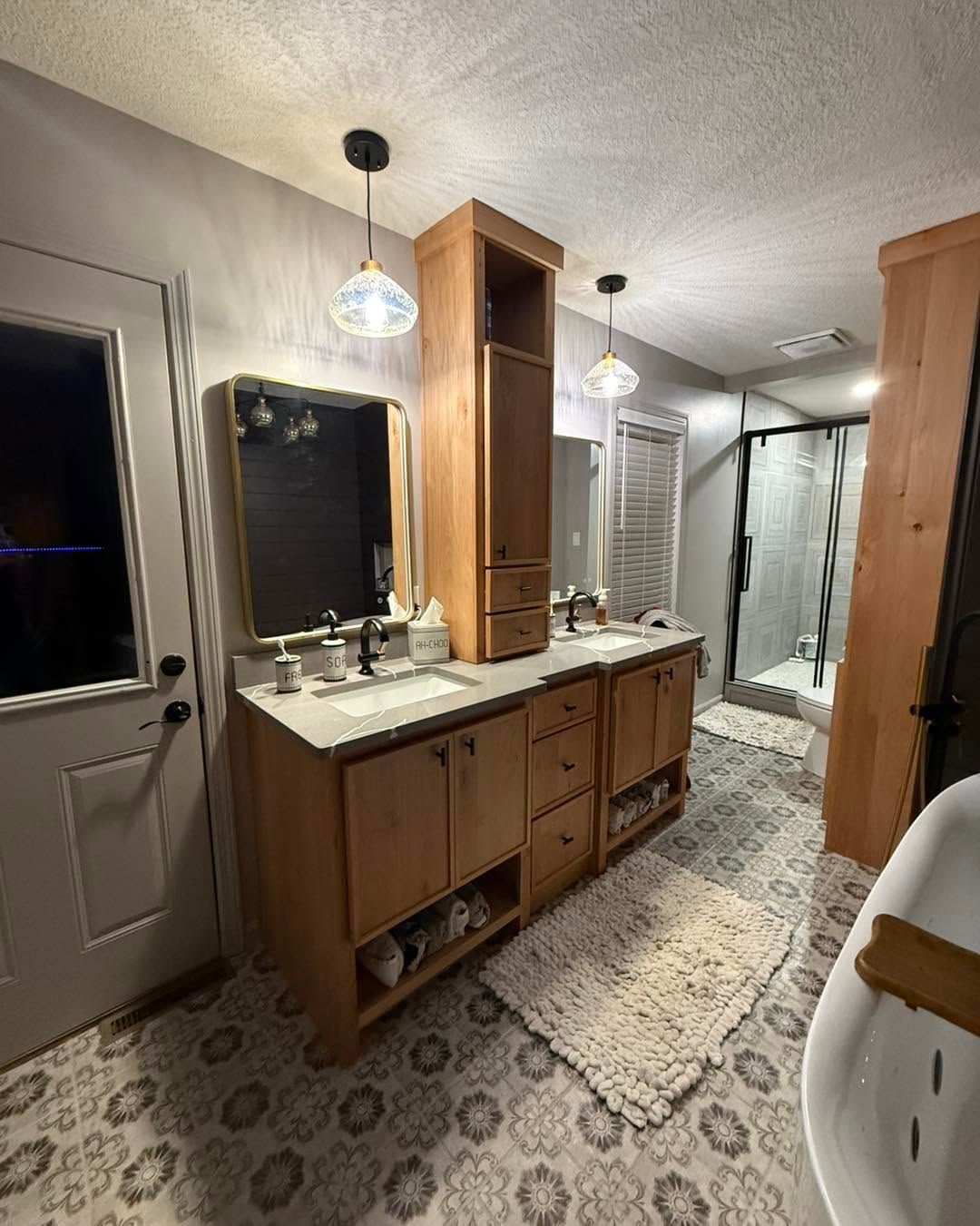 Bathroom with double vanity, wood cabinets, white counters, patterned tile floor, and glass shower.