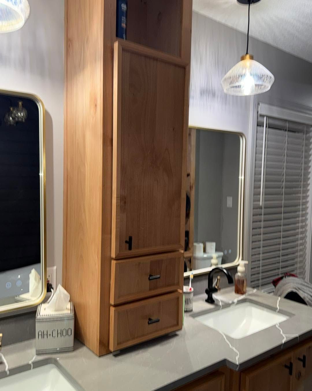 Bathroom vanity with wood cabinet, white sink, mirror, and pendant lights beside a window