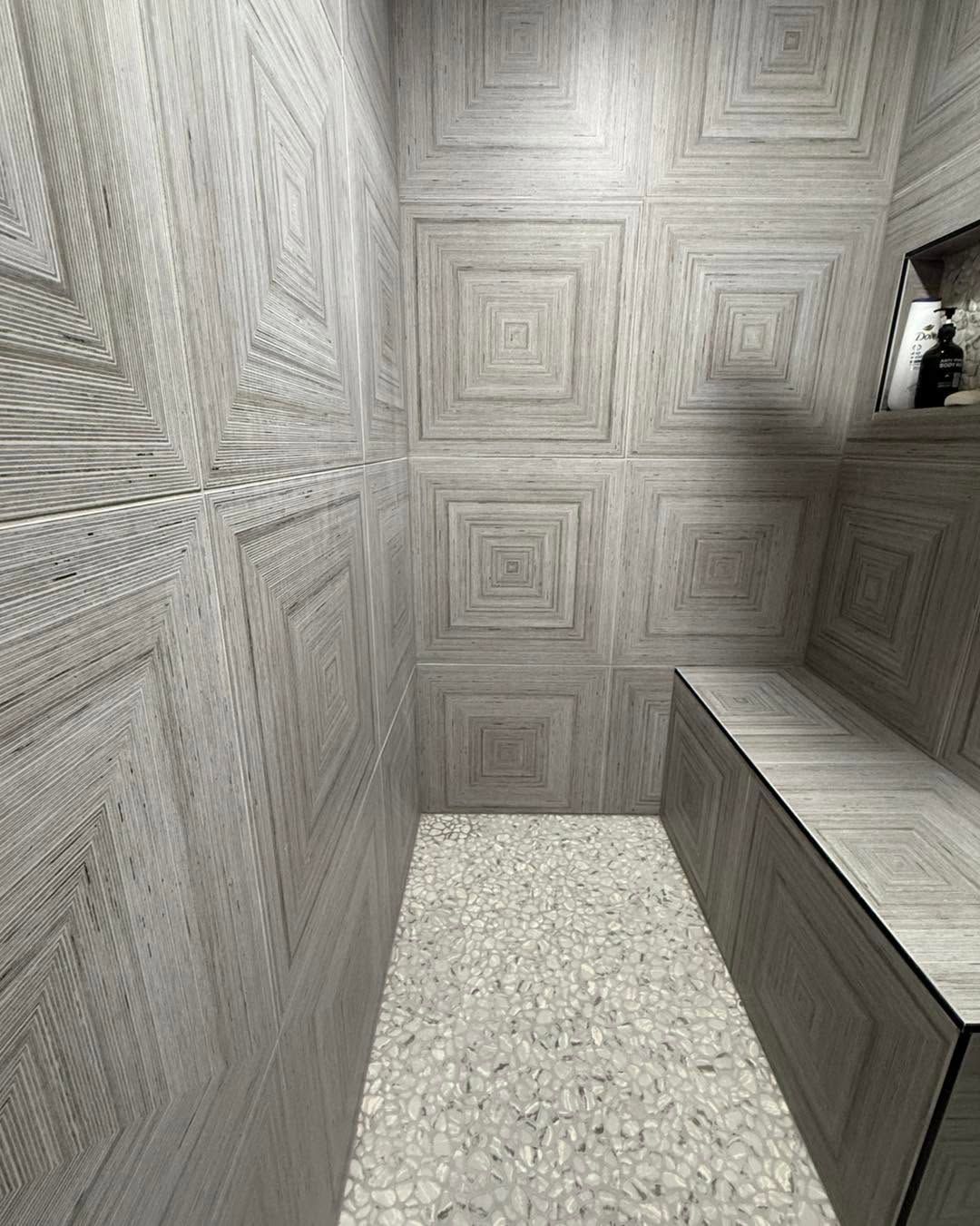 Narrow stone corridor with patterned gray walls, a gravel floor, and a raised ledge on the right.