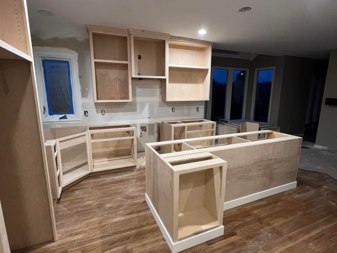 Unfinished kitchen with light wood cabinets and island frames in a modern room under construction