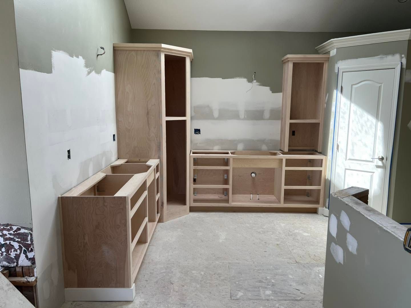 Unfinished room with built-in wooden cabinets, white walls, and a door on the right.