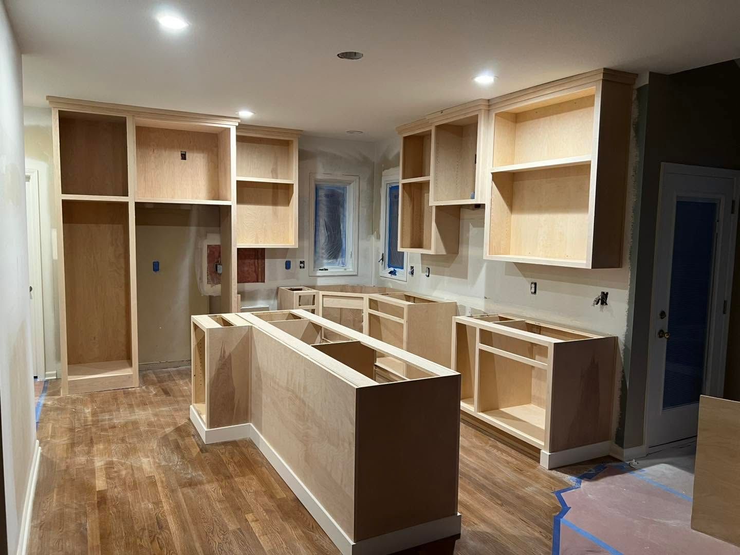 Partially finished kitchen with light wood cabinets, white countertops, and an island under construction