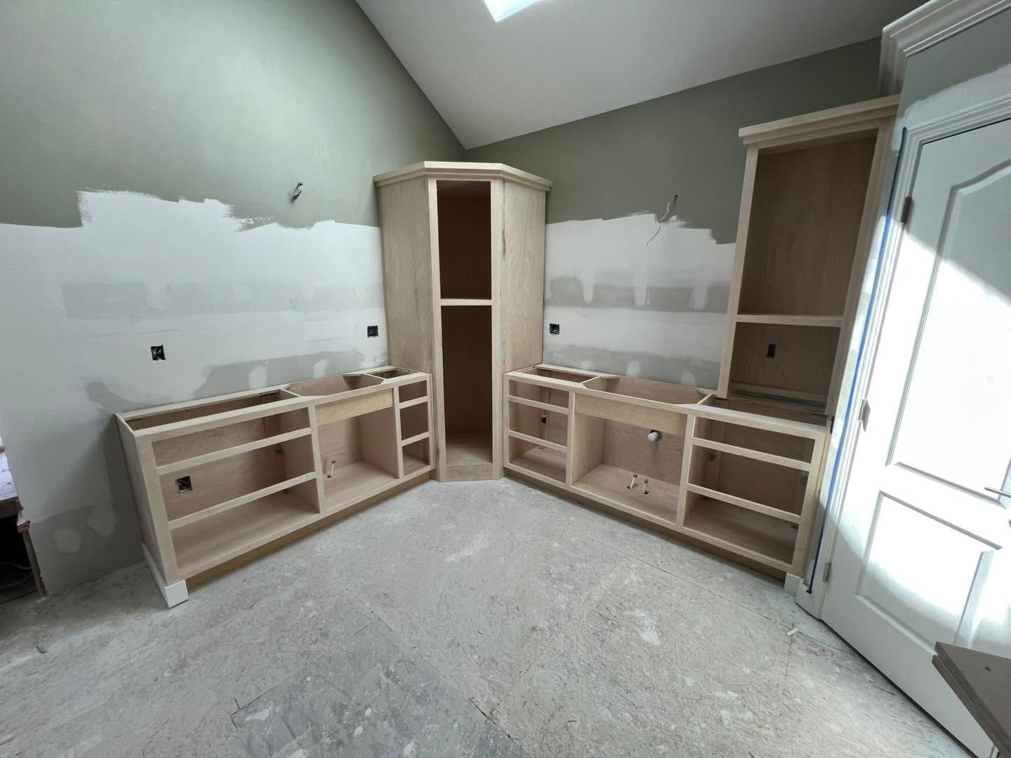 Unfinished room with built-in wood cabinets and shelves along two walls, white trim, and drywall patching.