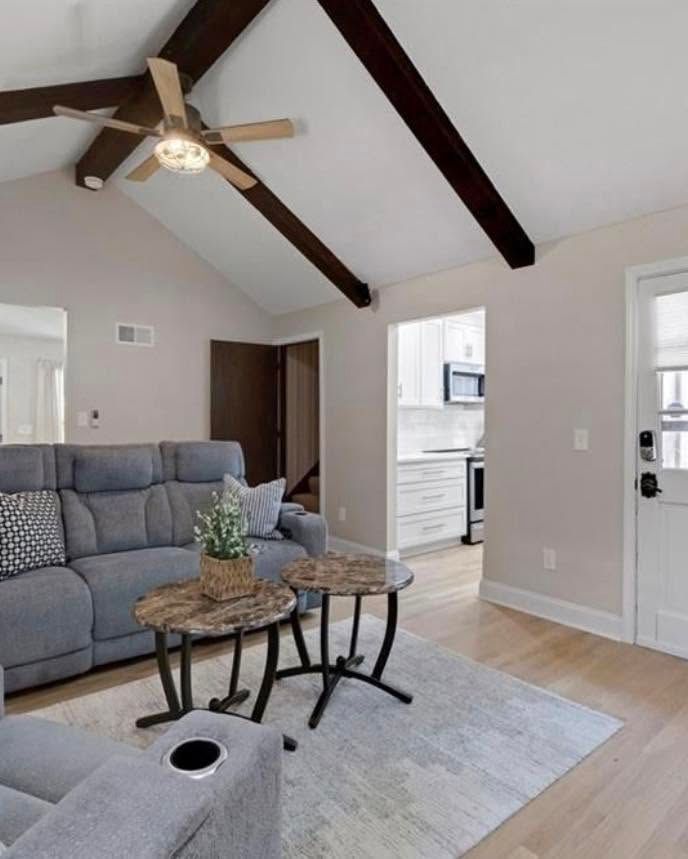 Bright living room with gray sofa, coffee tables, ceiling fan, and doorway to a kitchen.