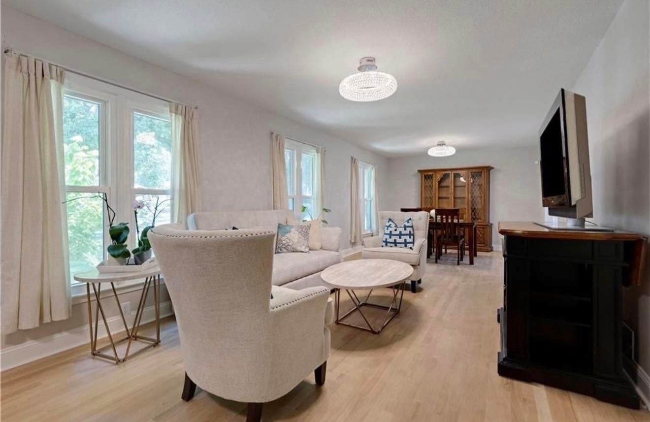 Bright living room with beige chairs, white sofa, wood floors, and large windows overlooking a dining area