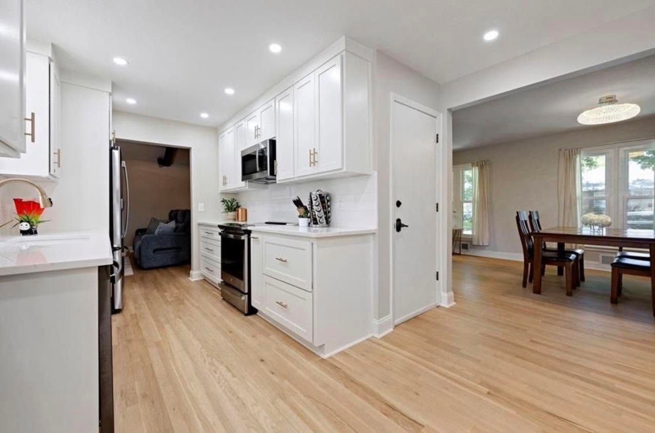Bright white kitchen with light wood floors opening to a dining room and entryway