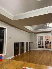 Empty modern living room with hardwood floors, beige walls, recessed ceiling lights, and a large windowed wall.