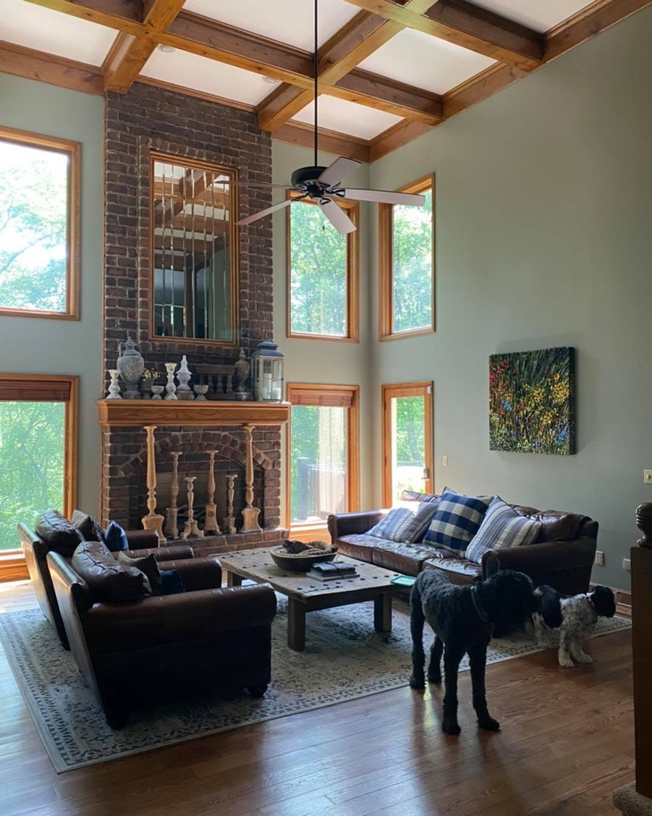 Bright living room with high wood ceiling, brick fireplace, sofas, and a black dog standing on the floor