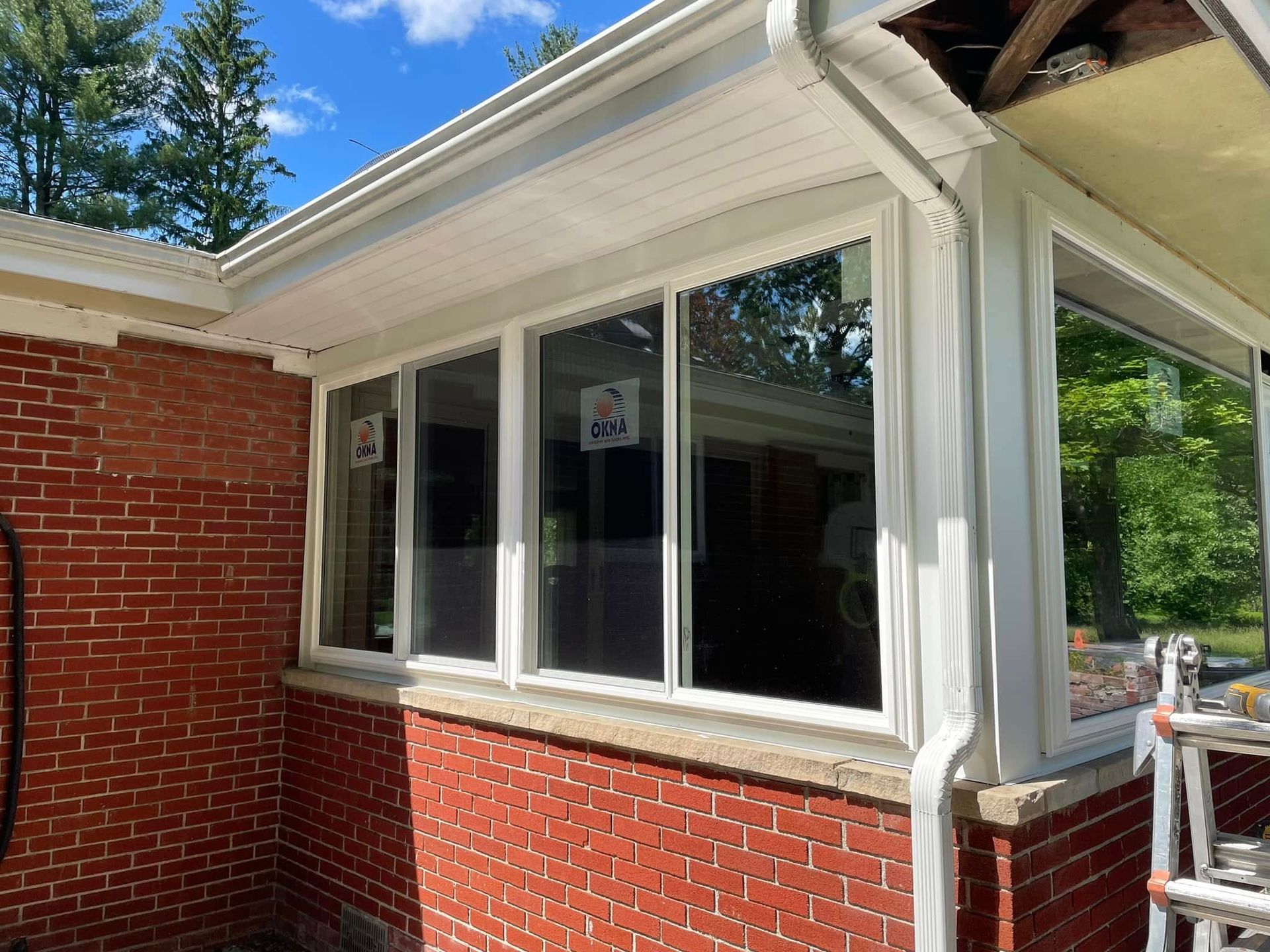 Brick building exterior with white-framed windows, gutters, and siding against a blue sky.