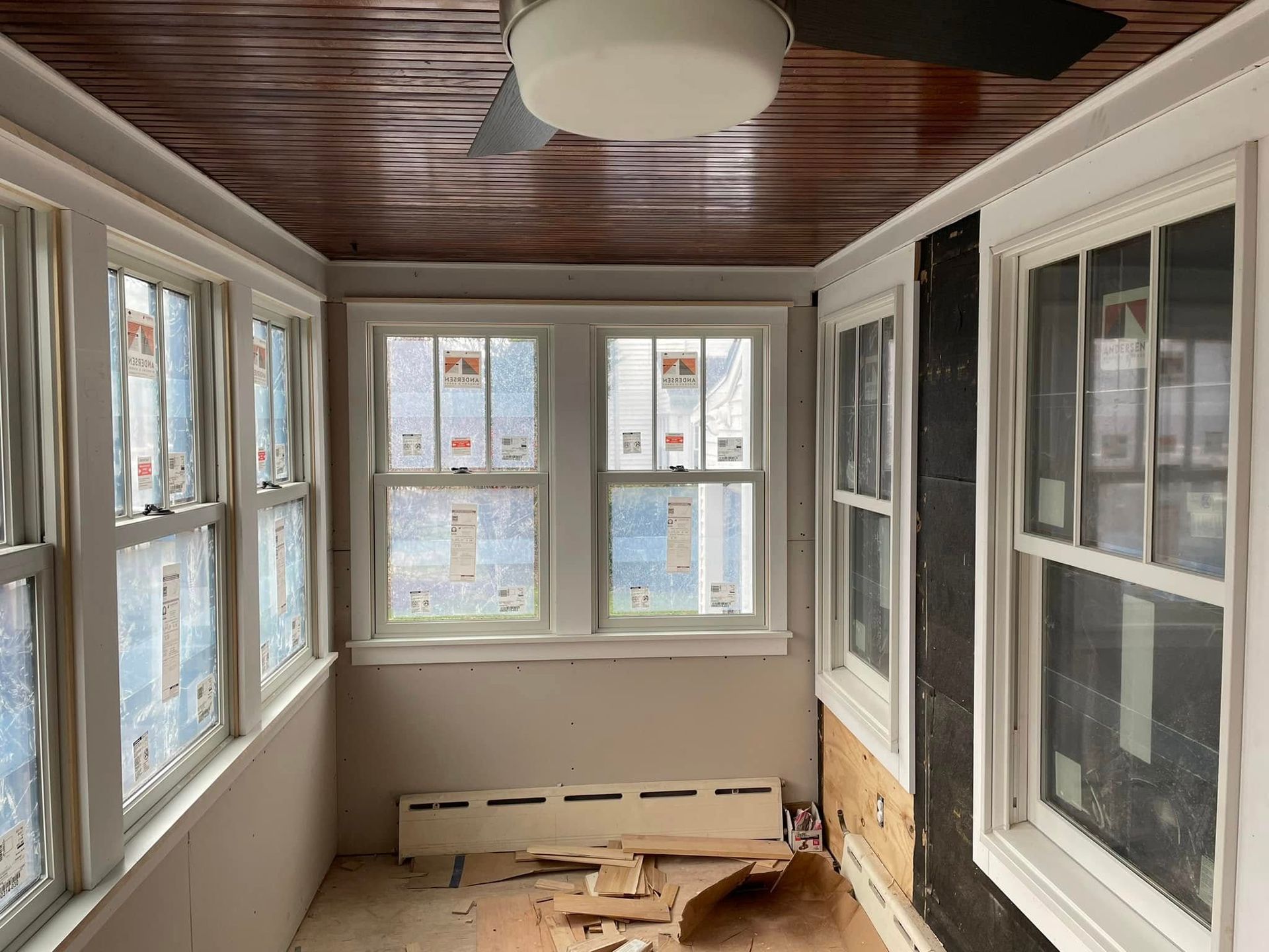 Sunroom interior with multiple windows, wooden ceiling and exposed wall, unfinished.
