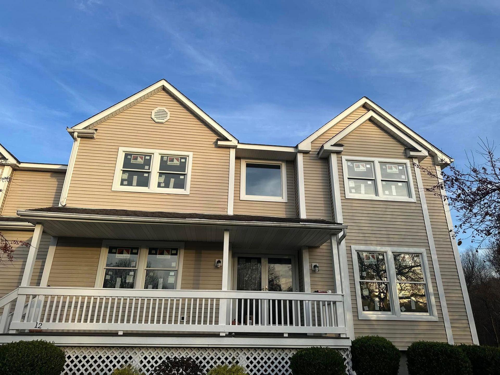Two-story beige house with white trim, porch, and blue sky.