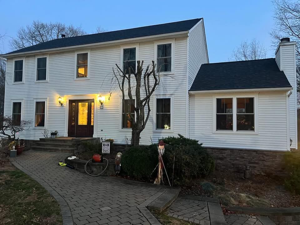 Two-story white house with dark roof and trim. Stone walkway leads to the front door, with early evening lighting.