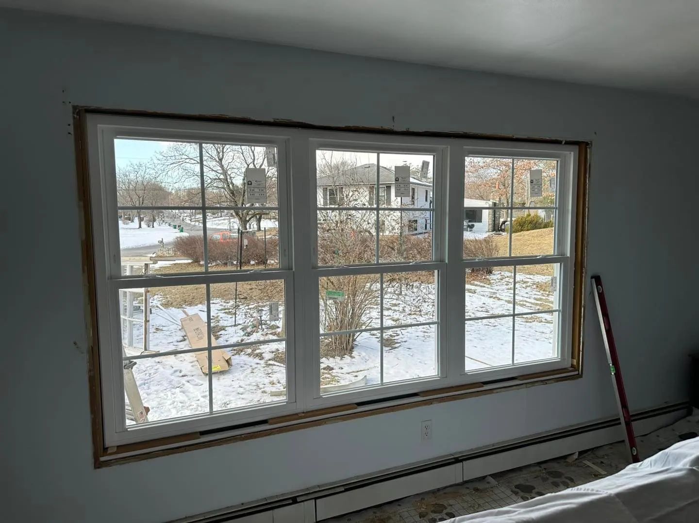 Large window overlooking a snowy yard, with a broom leaning against the wall inside.