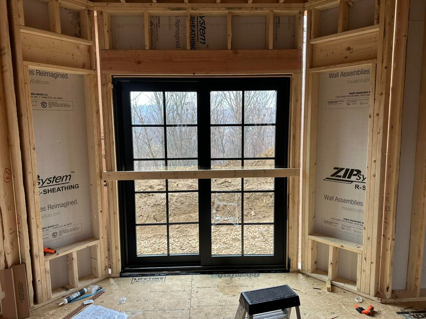 Interior view of a new construction window with wooden framing. Black window panes, unfinished walls and floor.